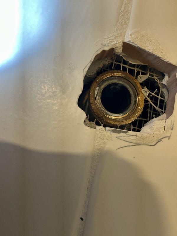 Repaired and remounted detached showerhead fixture in 56-year-old residence by reinforcing damaged wall substrate, installing new backing supports, and securing the brass pipe fitting. Removed deteriorated plaster and wire mesh, sealed exposed areas, and verified proper installation with leak testing to ensure fixture stability and prevent future detachment.