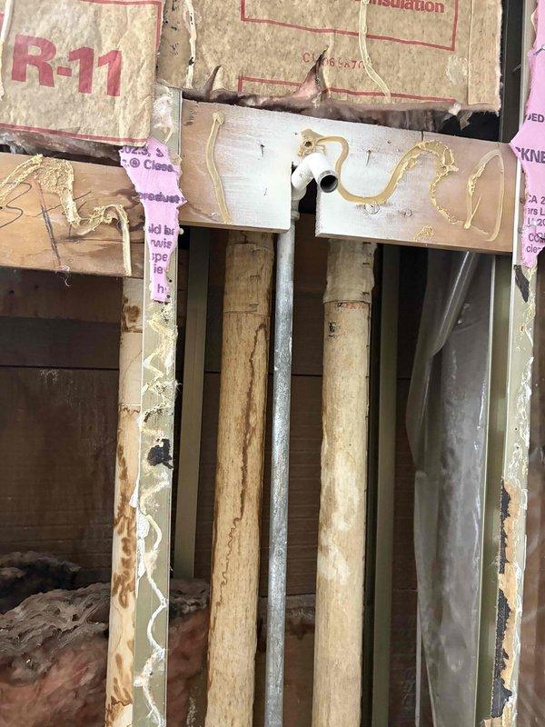 Inspected existing plumbing infrastructure for kitchen and bathroom remodel project. Documented exposed wall cavities showing R-11 insulation, horizontal white supply lines with sealant at connection points, and vertical drain stack with multiple PVC and copper pipes running through wooden framing. Assessment completed to determine requirements for upcoming plumbing modifications.