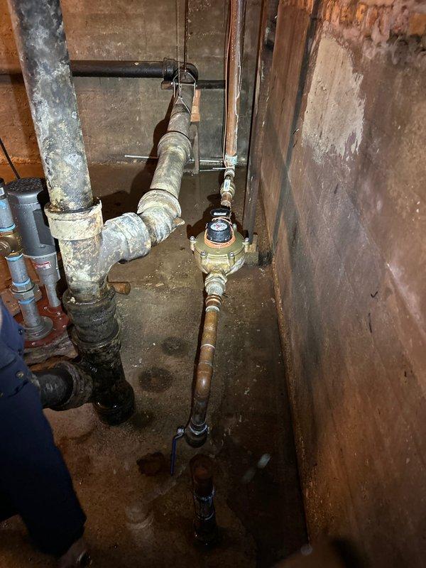 Responded to emergency main line burst at city connection point. Located significant water intrusion around copper pipe junction in basement utility area, with visible moisture on concrete floor. Repaired damaged section of main supply line and checked water meter functionality to ensure proper system operation after service completion.