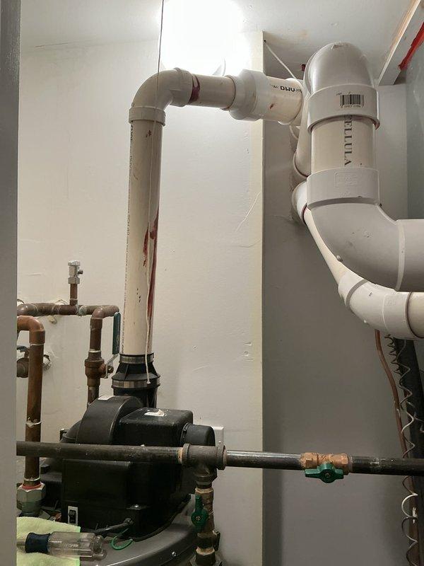 Responded to priority leak investigation in ceiling above hot water heater in mechanical closet. Inspected PVC drainage system suspected to be from unit above, identifying reddish-brown staining on horizontal pipe sections indicating the source of the leak. Documented the plumbing configuration including pump installation, copper supply lines, and PVC drainage components for comprehensive assessment.