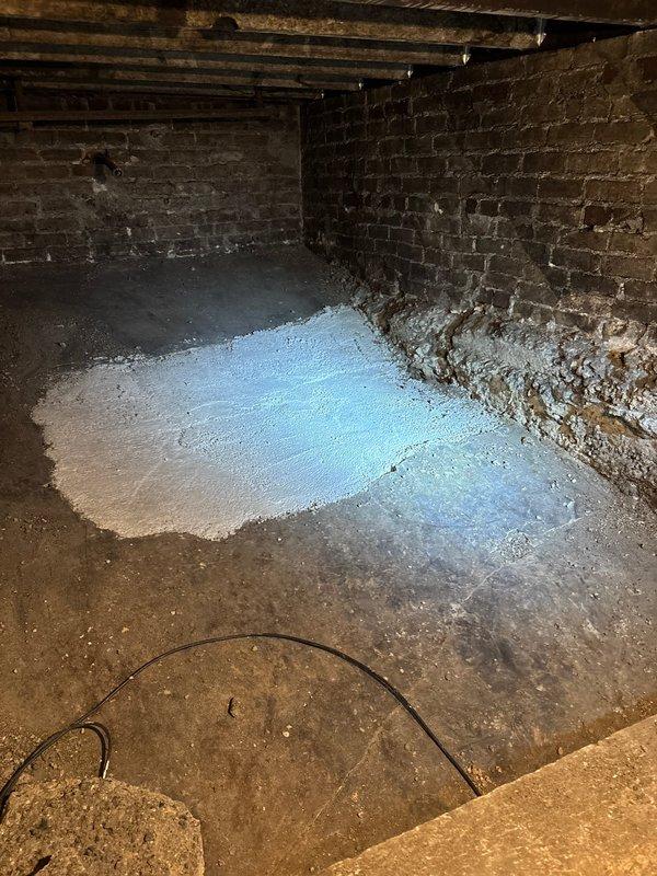 Performed inspection of 100-year-old main drain line with catch basin, documenting significant deterioration including brick wall degradation, standing water accumulation, and mineral deposits. Observed basement area showing signs of moisture intrusion with possible seepage through foundation walls, requiring further evaluation for hydro jetting service as requested.