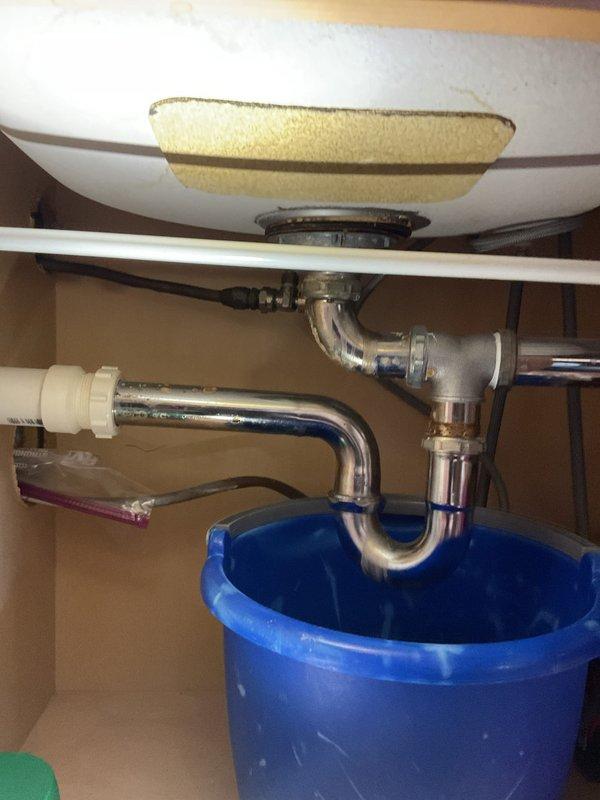 Responded to service call for double kitchen sink backup issue where both basins were draining into each other. Upon inspection, found significant blockage in the drain line. Disassembled P-trap and drainage assembly, cleared obstruction from the system, and verified proper flow restoration. Checked cabinet area for water damage from previous minor leaks as evidenced by staining on the cabinet floor.