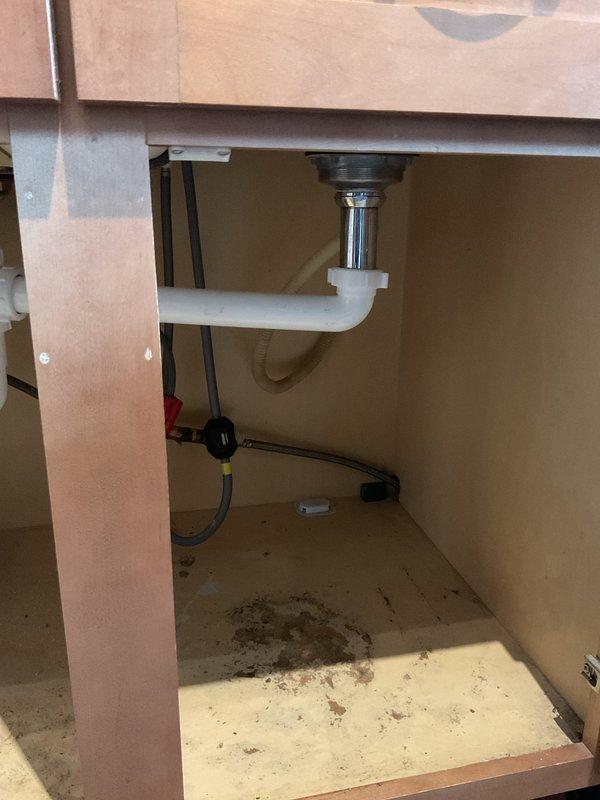Responded to service call for double kitchen sink backup issue where both basins were draining into each other. Upon inspection, found significant blockage in the drain line. Disassembled P-trap and drainage assembly, cleared obstruction from the system, and verified proper flow restoration. Checked cabinet area for water damage from previous minor leaks as evidenced by staining on the cabinet floor.