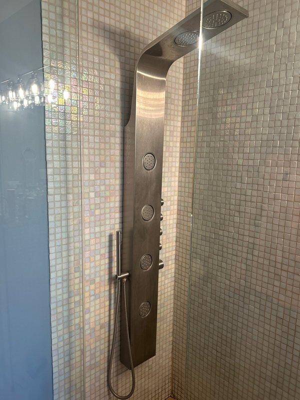 Returned for follow-up inspection of previously installed shower valve system and evaluated existing water heater for potential replacement. Confirmed proper installation and functionality of the stainless steel shower panel with multiple control buttons and rainfall shower head mounted on tiled wall. Water heater assessment completed; unit appears functional but replacement options were discussed based on age and efficiency considerations.