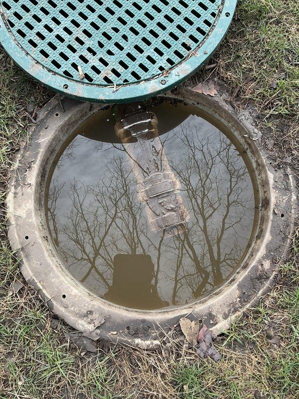 Responded to customer concern regarding excess water in backyard during rainfall. Inspected flood control system including manhole access point containing standing murky water and a circular drain pipe showing significant interior rust and water accumulation. Evaluation focused on drainage effectiveness and potential maintenance needs of both the flood control system and French drain.