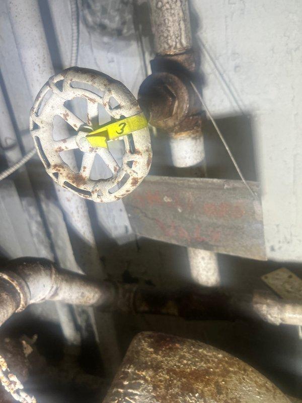 Conducted inspection of reported water leak at warehouse facility, locating source at corroded shut-off valve with significant oxidation visible on connecting pipes and fittings. Accessed blue utility manhole to verify water line configuration and assess underground components. Documented condition of deteriorating infrastructure with visible rust damage for comprehensive repair planning.