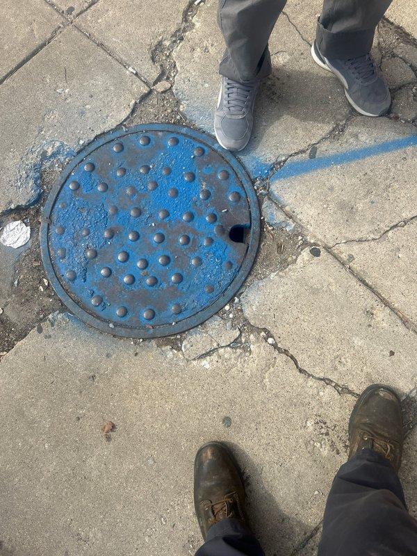 Conducted inspection of reported water leak at warehouse facility, locating source at corroded shut-off valve with significant oxidation visible on connecting pipes and fittings. Accessed blue utility manhole to verify water line configuration and assess underground components. Documented condition of deteriorating infrastructure with visible rust damage for comprehensive repair planning.