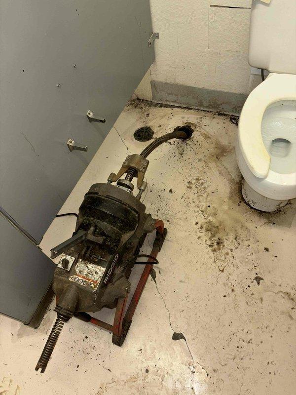 Responded to commercial facility with multiple toilets clogged and backing up through floor drain. Deployed heavy-duty drain snake/auger machine to clear severe blockage in main sewer line. Inspection of access shaft revealed significant corrosion, mineral buildup, and standing water, indicating potential need for future pipe maintenance or replacement.
