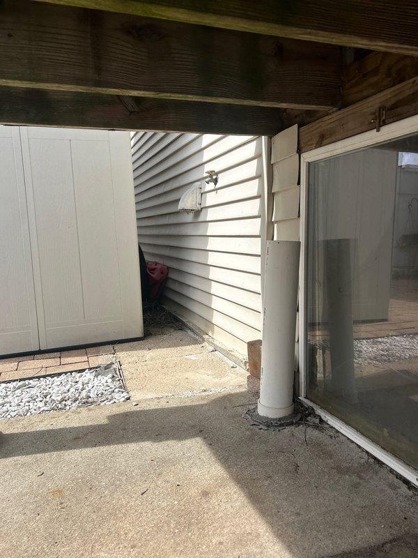 Conducted thorough inspection and provided estimate for catch basin cleaning service. Examined drainage system including deck area with circular concrete opening and connected white flexible duct/hose. Assessed associated components including downspout connection and surrounding drainage infrastructure under wooden deck structure.