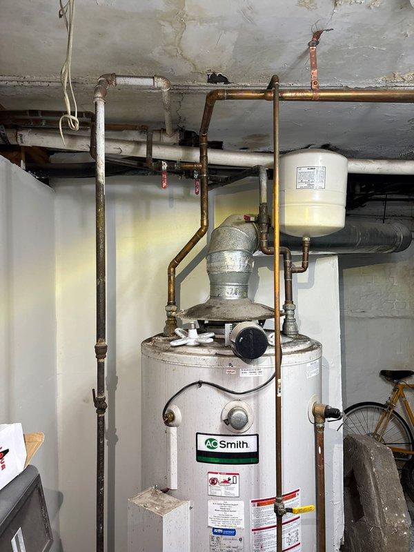 # Water Heater Replacement - Commercial Building

Responded to emergency service call for failed water heater in 6-unit commercial building. Upon arrival, assessed existing A.O. Smith water heater that had burst, causing immediate need for replacement to restore hot water service to all units. Documented existing installation including copper supply and distribution piping, expansion tank configuration, and gas line connections. Evaluated utility room conditions including overhead plumbing infrastructure, existing pipe corrosion, and available workspace for equipment replacement. Prepared comprehensive estimate for complete water heater replacement including removal of failed unit, installation of new appropriately-sized commercial water heater, reconnection of all water supply lines, gas line connections, expansion tank evaluation and replacement if necessary, and restoration of hot water service to building. Estimate includes all necessary materials, permits, and code-compliant insta