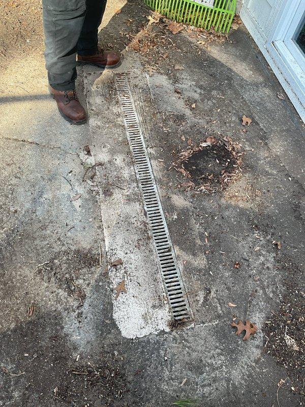 # Job Description

Responded to service call for backed-up exterior drain system. Upon arrival, located linear trench drain with metal grate installed in concrete patio area adjacent to sliding glass door entry. Drain showed visible signs of water backup and debris accumulation around grate openings.

Performed rodding service on exterior drainage line to clear obstruction causing backup. Inserted drain cable through grate openings and worked through blockage in underground drainage pipe. Removed accumulated organic debris, sediment, and buildup restricting water flow. Verified proper drainage function by testing water flow through system after clearing obstruction.

Inspected drainage grate and surrounding concrete surface for damage. Noted weathered concrete conditions and typical organic debris accumulation but found no structural issues requiring immediate attention. Grate remained securely in place with proper alignment for continued function.

Service restored normal drainage ope