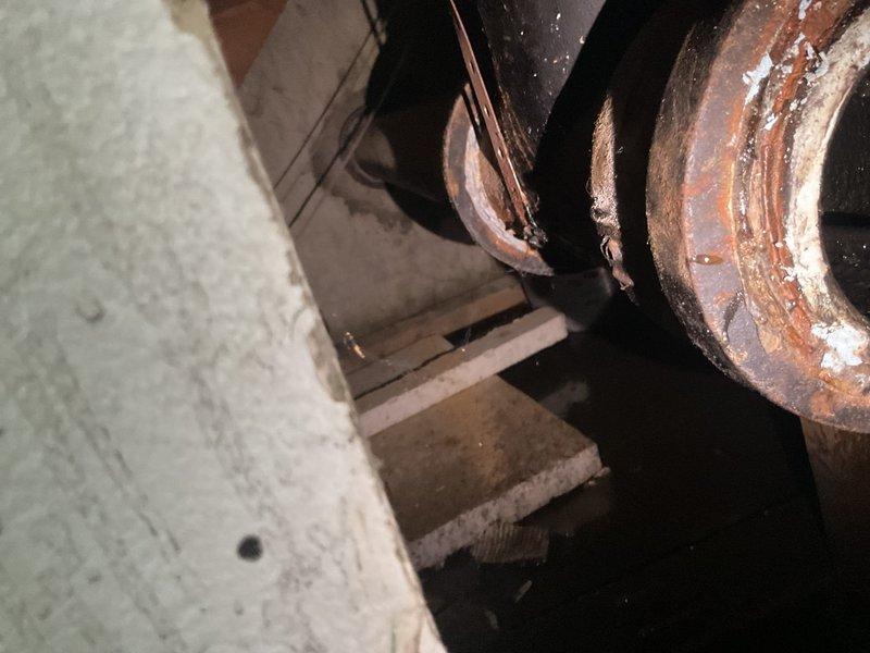 # Plumbing Estimate - Sump Pump Service Report

Responded to service call for blocked sewer stack causing water discharge issues when sump pumps were activated. Upon inspection, discovered severely corroded circular metal components and piping within confined mechanical space, with extensive rust, oxidation, and mineral deposits indicating prolonged moisture exposure. Performed wall access to expose interior plumbing infrastructure, revealing heavily corroded metal pipe with dark residue and moisture accumulation, deteriorated surrounding building materials, and compromised wooden framing members with visible staining, confirming drainage system failure requiring comprehensive repair estimate.
