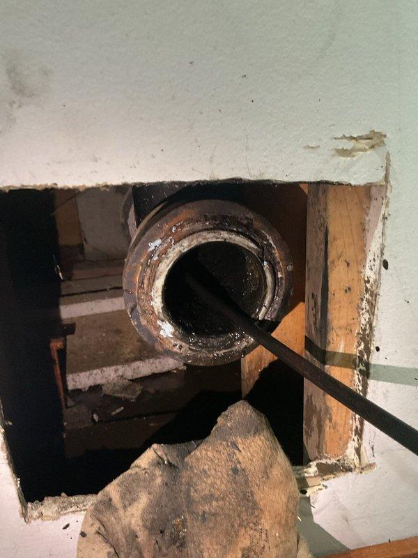 # Plumbing Estimate - Sump Pump Service Report

Responded to service call for blocked sewer stack causing water discharge issues when sump pumps were activated. Upon inspection, discovered severely corroded circular metal components and piping within confined mechanical space, with extensive rust, oxidation, and mineral deposits indicating prolonged moisture exposure. Performed wall access to expose interior plumbing infrastructure, revealing heavily corroded metal pipe with dark residue and moisture accumulation, deteriorated surrounding building materials, and compromised wooden framing members with visible staining, confirming drainage system failure requiring comprehensive repair estimate.