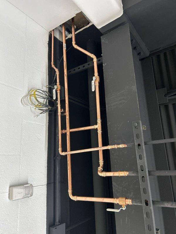 # Plumbing Service Report

Responded to a morning service call for plumbing repair assessment. Upon inspection, identified water damage and deterioration at the base of existing plumbing installation, evidenced by significant staining on wooden platform and surrounding concrete floor, indicating previous or ongoing moisture intrusion from plumbing connections. Documented existing copper piping system and associated fixtures, including brass valve connections and PVC drainage components in utility area. Provided customer with repair recommendations to address water damage concerns and ensure proper system operation.