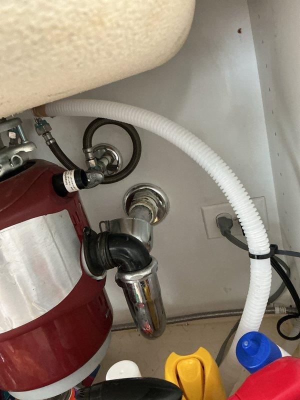# Plumbing Estimate - Fixture Completion

Conducted on-site assessment of kitchen sink plumbing system during scheduled building shutdown window. Documented existing KitchenAid garbage disposal installation, P-trap drainage assembly, and associated supply line connections for estimate preparation. Photographed under-sink cabinet configuration including disposal unit mounting, corrugated discharge hose routing, chrome-finished drain components, and electrical connections to provide comprehensive documentation for fixture replacement or repair proposal.