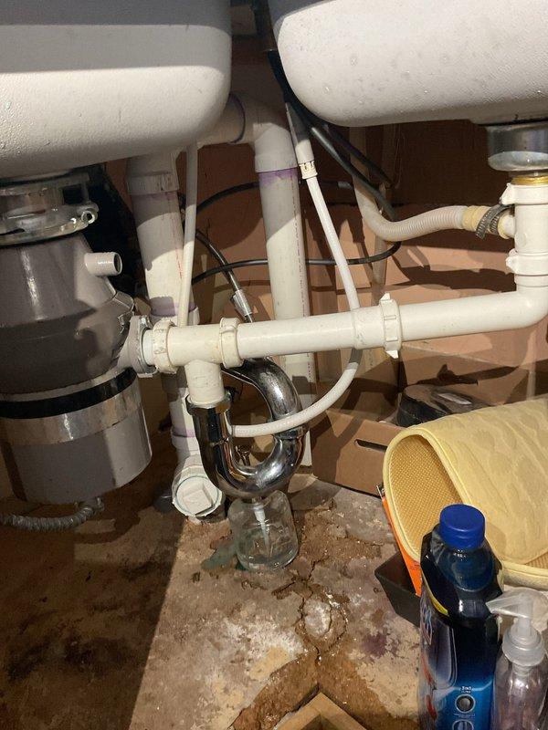 Responded to service call for multiple plumbing issues including a basement toilet that was not flushing properly and gurgling when upstairs toilet was flushed, indicating a potential venting or drainage obstruction. Inspected and diagnosed the toilet drainage system and venting configuration. Additionally assessed a first floor bathroom shower mixer valve that was making noise when in the off position, which stopped when adjusted, suggesting internal valve component wear or water hammer issues. Evaluated the first floor kitchen plumbing system, which included a garbage disposal, dishwasher, and dual sink configuration. Upon inspection, identified that the existing disposal installation and drain connections did not meet current plumbing code requirements. Documented the under-sink plumbing assembly showing non-compliant configuration with improper venting and drainage connections. Provided estimate for garbage disposal replacement with proper code-compliant installation including appr