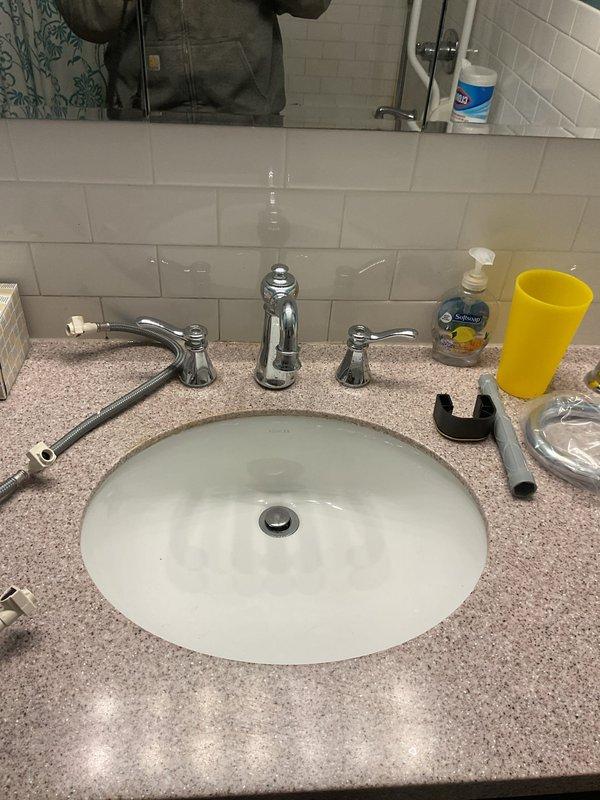 Replaced customer-supplied three-piece chrome faucet assembly on bathroom vanity with undermount sink and granite countertop. Removed existing faucet, installed new deck-mounted faucet with central spout and dual lever handles, connected supply lines, tested for proper operation and verified no leaks.