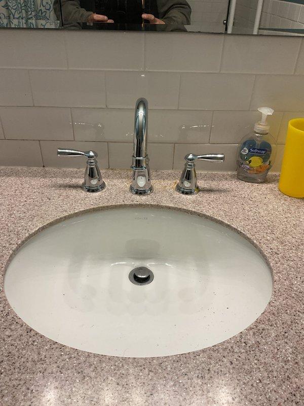 Replaced customer-supplied three-piece chrome faucet assembly on bathroom vanity with undermount sink and granite countertop. Removed existing faucet, installed new deck-mounted faucet with central spout and dual lever handles, connected supply lines, tested for proper operation and verified no leaks.