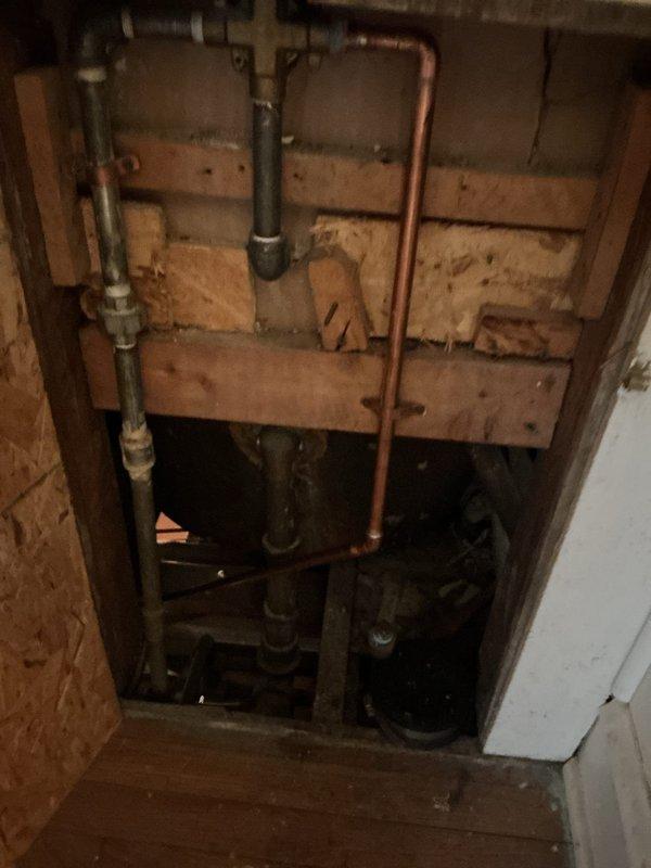 Responded to complaint of no water flow from shower with issue progressively worsening over one year period. Accessed plumbing infrastructure through exposed wall cavity to investigate potential faucet malfunction versus hot water supply problem. Inspected galvanized, copper, and black iron piping systems running vertically and horizontally through basement utility space. Identified significant corrosion on gray horizontal supply pipe at valve connection point, with visible rust accumulation compromising water flow. Examined multiple pipe junctions, fittings, and valve assemblies within the exposed plumbing network. Documented condition of aged infrastructure including corroded galvanized piping, copper supply lines, and associated mechanical connections to determine root cause of diminished water pressure affecting shower fixture.