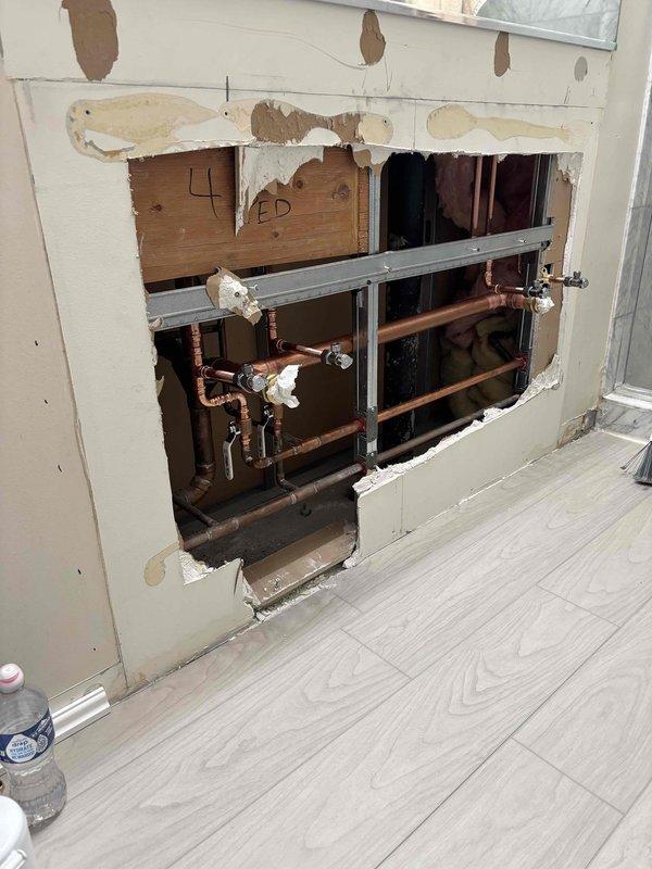 Accessed plumbing system through interior wall to address water damage and pipe concerns. Removed section of drywall to expose copper supply lines, shut-off valves, and support infrastructure. Identified water staining on wall surface and evaluated pipe connections and fittings for potential leaks or failures requiring repair.