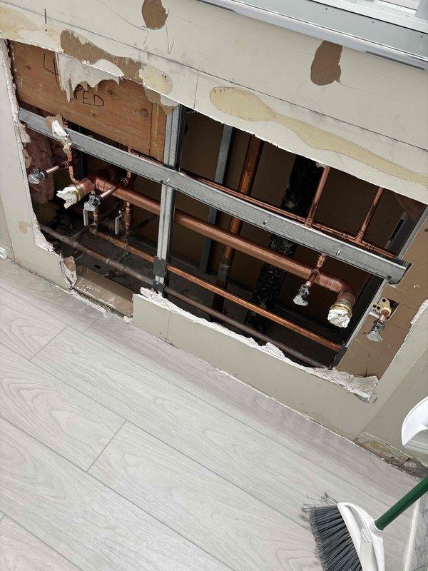 Accessed plumbing system through interior wall to address water damage and pipe concerns. Removed section of drywall to expose copper supply lines, shut-off valves, and support infrastructure. Identified water staining on wall surface and evaluated pipe connections and fittings for potential leaks or failures requiring repair.