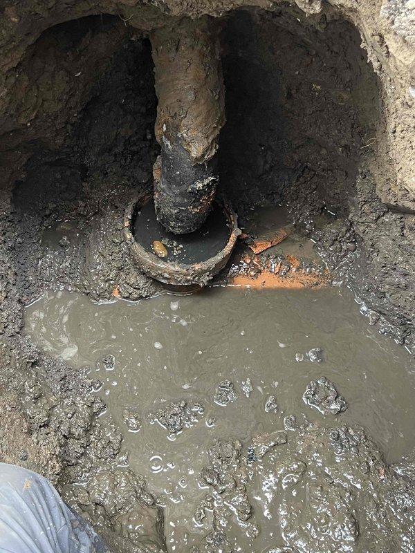 Conducted comprehensive drain and sewer system assessment at residential property requiring urgent attention. Inspection revealed severely deteriorated vertical sewer pipe in excavated access point with extensive corrosion, rust damage, and structural degradation. Standing water with sediment accumulation observed at base of excavation, indicating drainage issues and potential system failure. Corroded metal fittings and connections surrounding main pipe showed advanced deterioration requiring replacement.

Documented conditions in side yard access corridor between structures where active excavation work exposed underground utilities. Area secured with caution tape and plywood covering for safety during assessment. Evidence of recent excavation work visible along concrete walkway with exposed soil and gravel placement. Downspout and drainage components on building exterior evaluated as part of comprehensive system review.

Photographed all critical components including corroded pipe inf