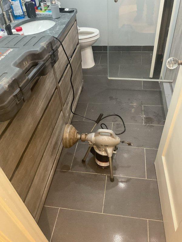 Responded to service call for drain maintenance requiring two-person crew with ladder access. Upon arrival, accessed and cleared the drain system in the modern bathroom featuring herringbone-tiled shower with linear center drain. Successfully completed drain servicing work, ensuring proper water flow and drainage function throughout the shower and bathroom plumbing system.