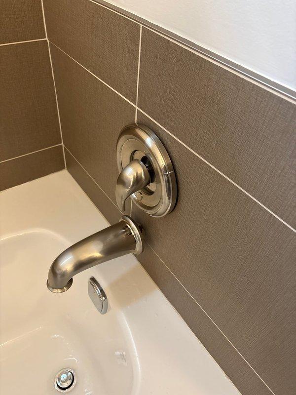 Responded to service call for bathtub leak causing water damage to ceiling below. Performed thorough inspection of tub fixtures, including brushed nickel spout, single-handle mixing valve, and handheld shower assembly mounted on tiled surround. Located source of leak at tub spout connection point where water was penetrating behind tile wall and migrating downward through ceiling cavity. Removed escutcheon plate to access valve body and confirmed improper seal at spout threaded connection. Applied appropriate sealant and reinstalled fixtures to manufacturer specifications, ensuring watertight connection. Verified repair by running water at full pressure and checking for moisture penetration. Documented existing bathroom installation with photographic evidence showing tile work, fixture placement, and completed repair.
