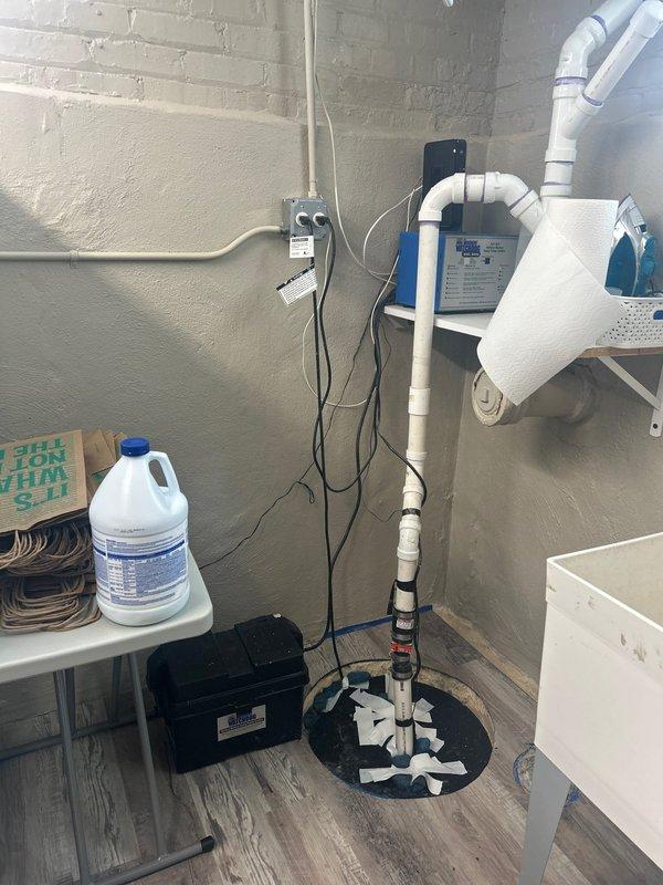 Conducted on-site assessment for sump pump and battery backup system installation in residential basement utility area. Evaluated existing sump pump configuration with white PVC discharge piping and circular sump basin currently installed in floor. Inspected overhead drainage routing and examined available space for potential battery backup integration. Documented current system layout including electrical connections, shelving placement, and accessibility constraints within the utility closet area. Provided comprehensive quote for new sump pump installation with battery backup system to ensure continued operation during power outages.
