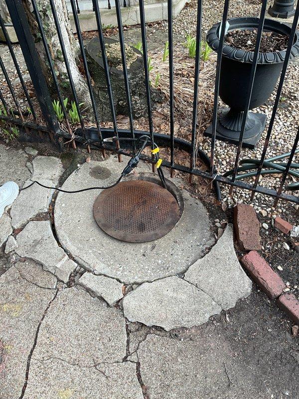 Responded to a water draining issue in the front sewer line of a century-old residence that had been experiencing drainage problems for two days. Upon arrival, inspected the exterior drain grate located in the patio walkway area, which showed significant rust deterioration and potential blockage concerns. The rusted metal grate was embedded in heavily cracked concrete with visible structural deterioration around the drain opening.

Conducted a thorough assessment of the drainage system, including inspection of the lower-level exterior stairway access point where standing water and moisture accumulation were evident on the concrete landing. The presence of moss growth on the stairs and standing water at the base indicated chronic drainage issues and improper water flow from the upper drain system.

Utilized drain cleaning equipment to clear the blockage in the front sewer line, removing accumulated debris and sediment that had built up over time in the aging cast iron or clay pipe syste
