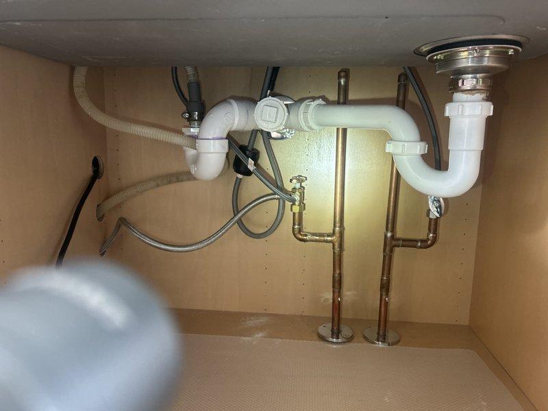 Technician responded to investigate reported kitchen drain leak but was unable to recreate the issue during inspection. Upon examination of the dual-basin kitchen sink plumbing system, noted standard white PVC P-trap configuration with connections to garbage disposal unit and secondary drain assembly. Basement ceiling below kitchen had already been opened for access to drain lines. Provided estimate for complete kitchen drain line replacement, as existing piping showed signs of age and potential failure points. Customer requested scheduling for drain system renovation work to prevent future leakage issues.