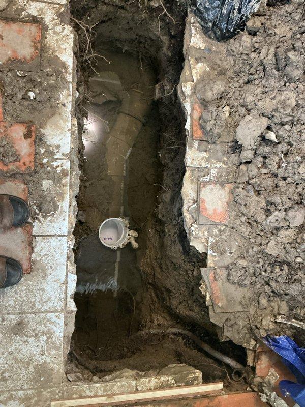 Responded to service call for sewer repair estimate where previous contractor had discontinued work after excavating approximately 4 feet down. Upon arrival, assessed existing excavation site revealing a water-filled trench with exposed sewer line and deteriorated surrounding flooring materials including terracotta tiles. Inspected utility access pit containing submersible pump with standing water and visible reflections indicating proper depth. Documented site conditions including muddy trench with visible debris, exposed white pipe fitting in center of excavation, and rusted metal collar surrounding pit access point. Evaluated scope of remaining work required to complete sewer line repair from current excavation depth, noting existing infrastructure condition and drainage system components. Prepared comprehensive estimate for continuation of sewer repair project based on observed site conditions and required remediation work.
