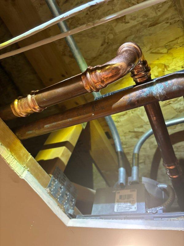 Responded to morning appointment for plumbing repair evaluation in basement utility area. Upon inspection, assessed copper supply line configuration with elbow fittings and associated piping infrastructure mounted to floor joists. Documented existing plumbing conditions including aged copper piping with oxidized patina, mounting brackets, and adjacent gray PVC drainage lines in unfinished ceiling space with exposed joists and insulation. Repair proposal was accepted and work authorization obtained to proceed with necessary plumbing modifications to the copper supply system.