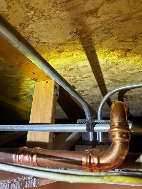 Responded to morning appointment for plumbing repair evaluation in basement utility area. Upon inspection, assessed copper supply line configuration with elbow fittings and associated piping infrastructure mounted to floor joists. Documented existing plumbing conditions including aged copper piping with oxidized patina, mounting brackets, and adjacent gray PVC drainage lines in unfinished ceiling space with exposed joists and insulation. Repair proposal was accepted and work authorization obtained to proceed with necessary plumbing modifications to the copper supply system.