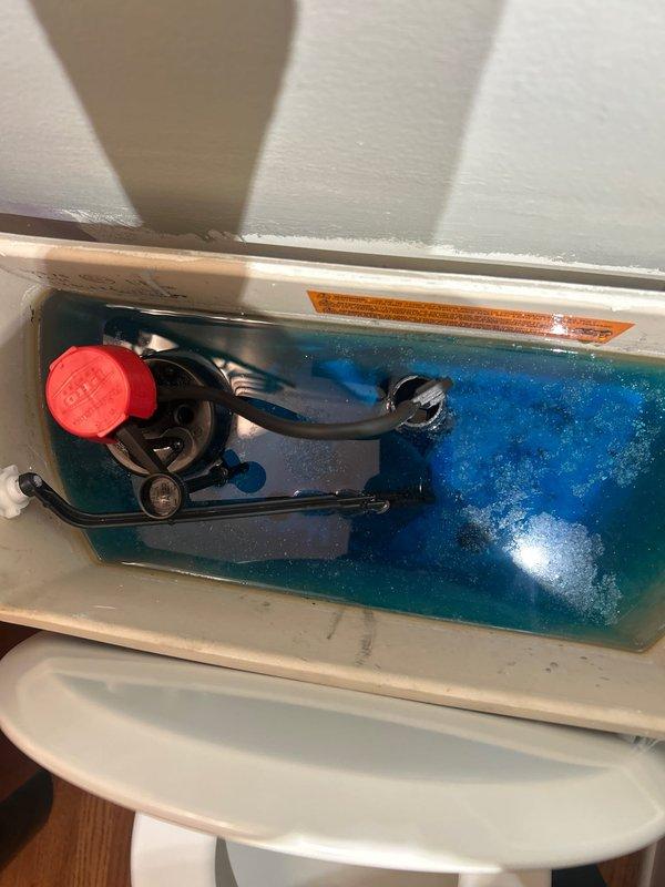 Responded to warranty callback for continuously running toilet that was previously serviced. Upon inspection, observed blue cleaning tablet in tank water and examined flush valve assembly with red float mechanism and black linkage components. Diagnosed issue with internal tank mechanisms causing constant water flow. Adjusted and tested flush valve operation to restore proper function and eliminate running water condition.
