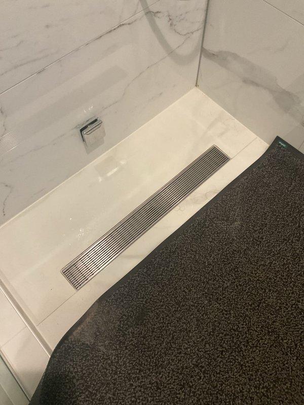 Responded to a completely clogged shower drain with no drainage. Removed and cleaned the linear drain grate and chrome drain strainer, extracting accumulated hair, soap residue, and debris causing the blockage. Tested water flow after clearing obstruction to confirm proper drainage was restored and all fixtures were functioning correctly.