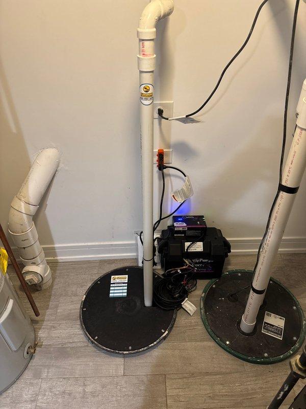 Installed a comprehensive radon mitigation and sump pump system in the basement utility area. The installation included vertical white PVC piping with proper elbow configurations running from floor to ceiling, two black circular sump pump cover plates installed flush with the flooring, and a radon fan monitoring device with digital display showing active operation. All electrical components were properly wired and routed along the wall, with appropriate warning labels affixed to the radon mitigation piping per code requirements.