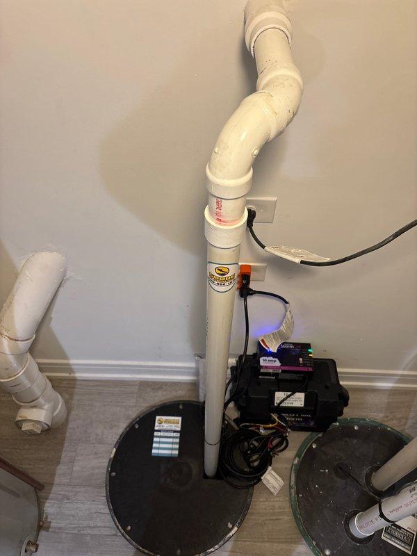 Installed a comprehensive radon mitigation and sump pump system in the basement utility area. The installation included vertical white PVC piping with proper elbow configurations running from floor to ceiling, two black circular sump pump cover plates installed flush with the flooring, and a radon fan monitoring device with digital display showing active operation. All electrical components were properly wired and routed along the wall, with appropriate warning labels affixed to the radon mitigation piping per code requirements.