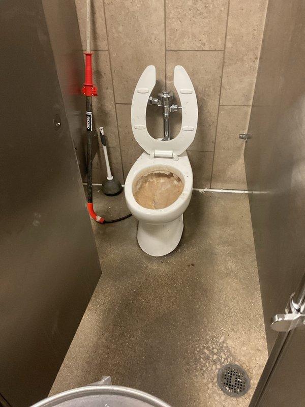 Responded to service call for clogged toilet and two urinals in commercial restroom facility. Upon arrival, found toilet bowl containing standing water with visible debris indicating complete blockage. Successfully cleared toilet obstruction using mechanical plunging methods, restoring proper flush function and drainage. Inspected and serviced both wall-mounted urinals, which were experiencing similar drainage issues. Placed urinals temporarily out of service with protective coverings during maintenance. Cleared blockages from urinal drain lines, tested flush valves and piping for proper operation, and restored both fixtures to full working condition. Verified all three fixtures were draining properly before completing service.