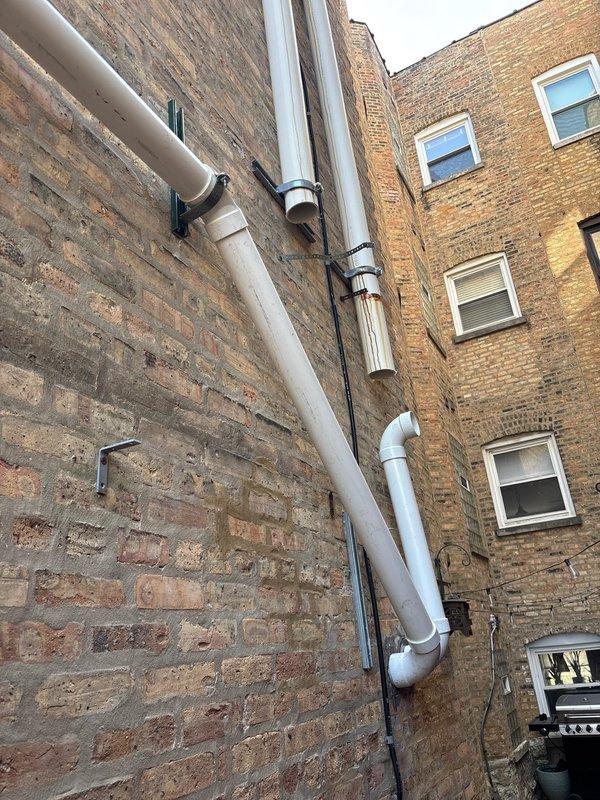 Completed inspection of exterior plumbing installation on multi-story brick building, including vertical drainage system and water heater venting. Documented existing PVC pipe configuration with mounting brackets and elbow joints along building exterior. Part ordered and available in shop for scheduled follow-up installation to complete the tanked water heater service.