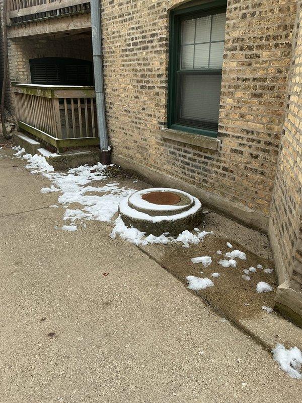 Conducted site assessment for flood control installation at a nine-unit commercial condominium building constructed directly adjacent to the sidewalk with no front yard available for traditional check valve placement. Evaluated the parkway area as an alternative installation location for backwater valve system, documenting existing conditions including utility access points, landscaping features, and building foundation proximity. Photographed site conditions to support permit application process for installing flood control device in the public right-of-way, as this represents the only viable option for protecting the property from sewer backup due to the building's setback constraints.