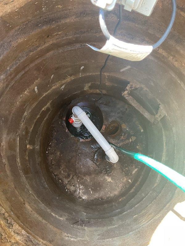 Responded to basement flooding complaint with suspected main line or sewer issue. Conducted thorough inspection of drainage system including interior plumbing access point and exterior sump pit. Accessed wall cavity to examine drain pipe assembly and connecting hardware, documenting exposed plumbing components and system configuration. Inspected concrete sump pit revealing standing water accumulation, existing PVC drainage pipe with coupling assembly, and overall system condition showing sediment buildup and moisture exposure patterns consistent with drainage concerns.