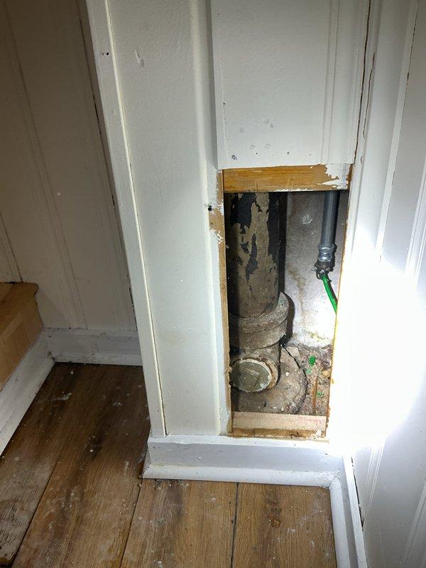 Responded to estimate request for suspected broken sewer line at bottom of toilet stack. Created access opening in white paneled wall to expose plumbing system and assess condition of drainage pipes. Investigation revealed gray PVC drain stack and associated plumbing components requiring evaluation for potential repair or replacement of compromised sewer line section.