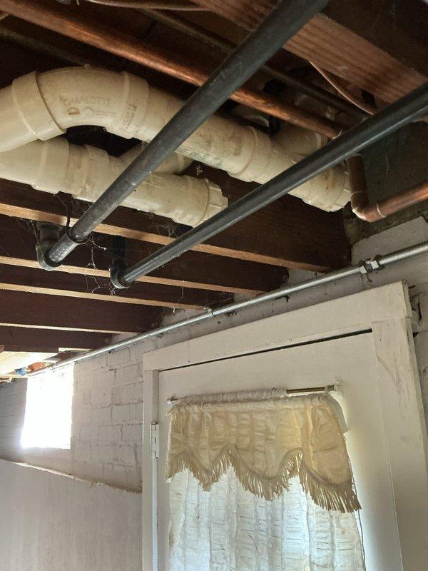 Responded to service call for potential radiator leak investigation. Conducted thorough inspection of basement utility area and exposed ceiling structure. Located active water leak source at wooden floor joist showing significant moisture damage and dark staining consistent with ongoing water infiltration. Identified compromised area above plumbing supply lines where water had been tracking down structural beam. Documented leak location with photographic evidence showing water-damaged joists, exposed PVC drain lines, copper supply lines, and HVAC ductwork in affected area. Traced leak pattern to determine origin point and extent of moisture penetration in ceiling structure. Provided property owner with findings and recommendations for necessary repairs to resolve active leak condition.