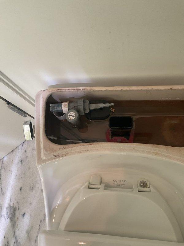 Responded to a multi-fixture plumbing service call involving three continuously running toilets, one non-flushing toilet requiring repair, a toilet needing re-sealing, a clogged shower drain, and a leaking kitchen faucet. Inspected and photographed the non-functional toilet, which was marked out of service, and documented the internal tank components showing mineral buildup and worn flush mechanism parts on a Kohler unit. Assessed flush valve assembly, flapper condition, and fill valve operation to determine necessary repairs for restoring proper function to all affected fixtures.