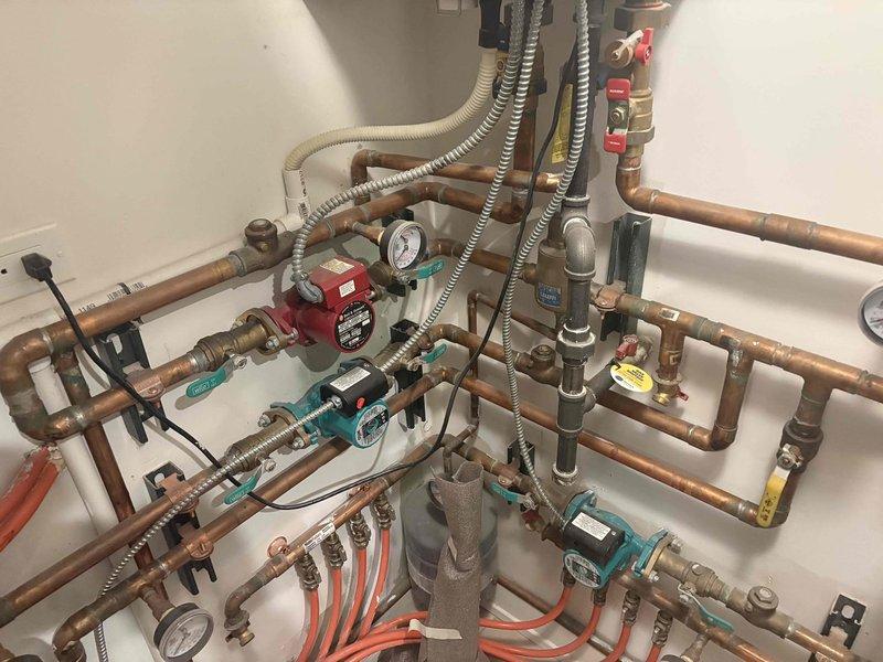 Responded to service call for boiler system displaying maintenance or repair error code. Upon arrival, inspected multi-zone hydronic radiant heating system with complex copper piping network, multiple circulator pumps, zone valves with actuators, and integrated pressure monitoring equipment. Evaluated system components including red circulator pump, teal-handled zone valves, brass shut-off valves, pressure gauges, and PEX tubing connections. Assessed electrical controls, wiring connections, and zone valve operations. Examined copper piping for proper flow, checked all pressure readings throughout the system, and verified circulator pump functionality. Documented existing system configuration showing professional installation with organized pipe routing, proper mounting brackets, and appropriate safety controls including expansion tank and multiple isolation points for system maintenance.