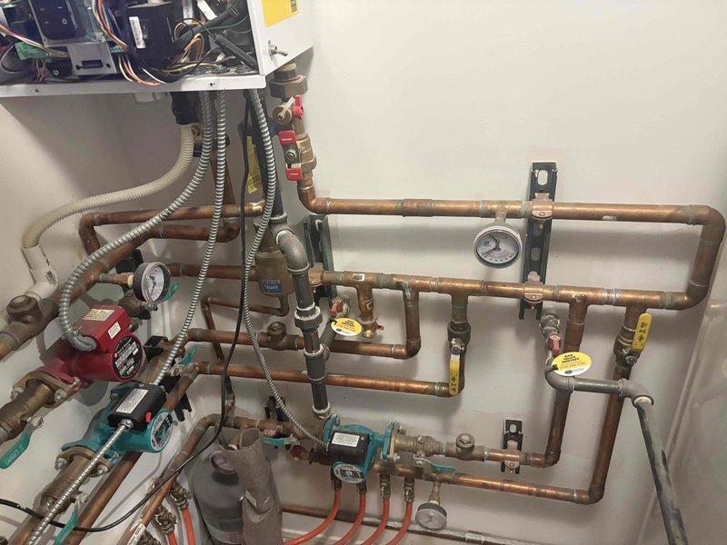 Responded to service call for boiler system displaying maintenance or repair error code. Upon arrival, inspected multi-zone hydronic radiant heating system with complex copper piping network, multiple circulator pumps, zone valves with actuators, and integrated pressure monitoring equipment. Evaluated system components including red circulator pump, teal-handled zone valves, brass shut-off valves, pressure gauges, and PEX tubing connections. Assessed electrical controls, wiring connections, and zone valve operations. Examined copper piping for proper flow, checked all pressure readings throughout the system, and verified circulator pump functionality. Documented existing system configuration showing professional installation with organized pipe routing, proper mounting brackets, and appropriate safety controls including expansion tank and multiple isolation points for system maintenance.