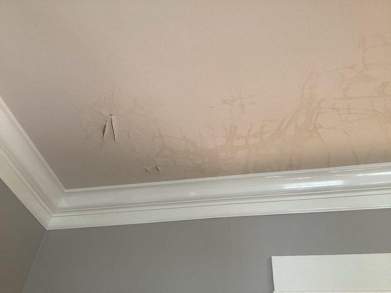 Investigated water damage on ceiling below shower and documented conditions. Inspection revealed significant water staining and discoloration on ceiling surface with irregular patterns indicating infiltration from above, along with moisture accumulation on copper piping components in the affected area. Photographed damaged areas and mechanical components for warranty documentation and further assessment of leak source.