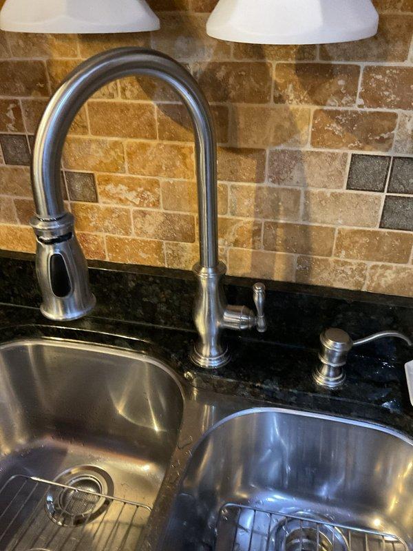 Responded to priority service call for leaking kitchen faucet. Upon arrival, performed comprehensive assessment of modern stainless steel pull-down spray faucet installed on double-bowl undermount sink with black granite countertop. Inspected faucet assembly, spray head mechanism, and mounting hardware from above-counter position. Examined under-sink plumbing connections, supply lines, and drain assembly including P-trap configuration and garbage disposal unit connections. Documented existing conditions with photographs showing faucet system, sink installation, and cabinet plumbing arrangement. Provided technical evaluation and recommendations regarding repair versus replacement options based on observed leak source and overall fixture condition.