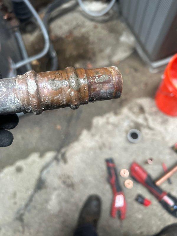 Responded to service call for reported leaking pipe requiring replacement. Upon arrival, conducted thorough inspection of exterior plumbing system adjacent to HVAC unit installation. Located source of leak at corroded copper pipe fitting showing advanced deterioration with significant oxidation, patina buildup, and moisture damage. 

Assessed copper piping assembly displaying mottled brown and green corrosion typical of prolonged water exposure and age-related degradation. Documented existing conditions through photographic evidence showing compromised pipe integrity at connection point. Evaluated surrounding plumbing infrastructure including conduit routing, drainage lines, and mounting configuration on concrete pad foundation.

Prepared comprehensive estimate for copper pipe replacement including affected fittings and connections. Estimate covers removal of deteriorated section, installation of new copper piping with proper fittings, and restoration of water-tight seal to eliminate a